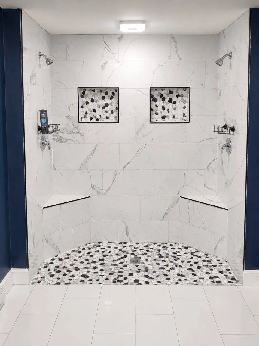 Tiled walk-in shower with dual shower heads, two recessed niches, corner benches and a pebble floor in a finished basement bathroom