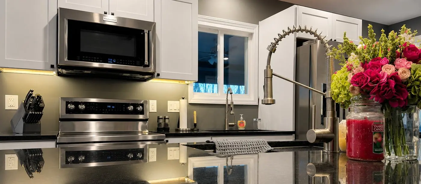 Detail of the finished Danville kitchen — the range, pull-down faucet and window reflected in the polished granite countertop, with flowers on the counter