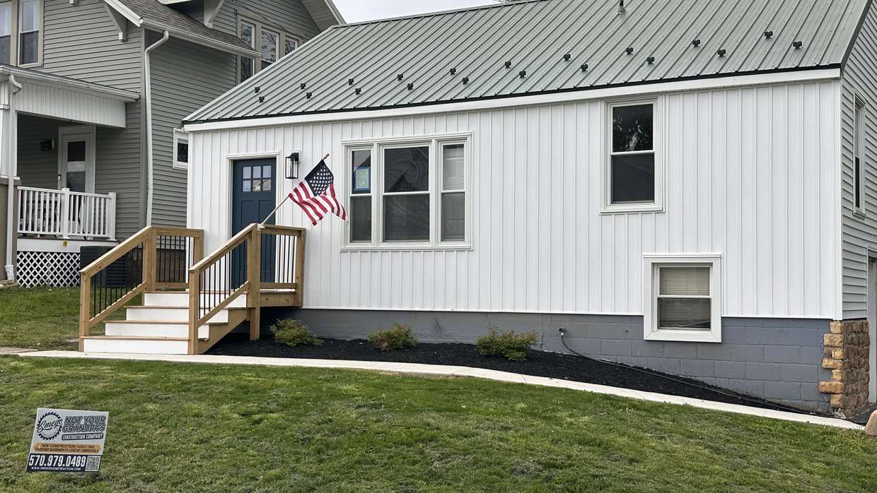 Finished whole-home renovation in Shamokin Dam, Pennsylvania — white siding, green standing-seam metal roof, new front steps and a regraded lawn