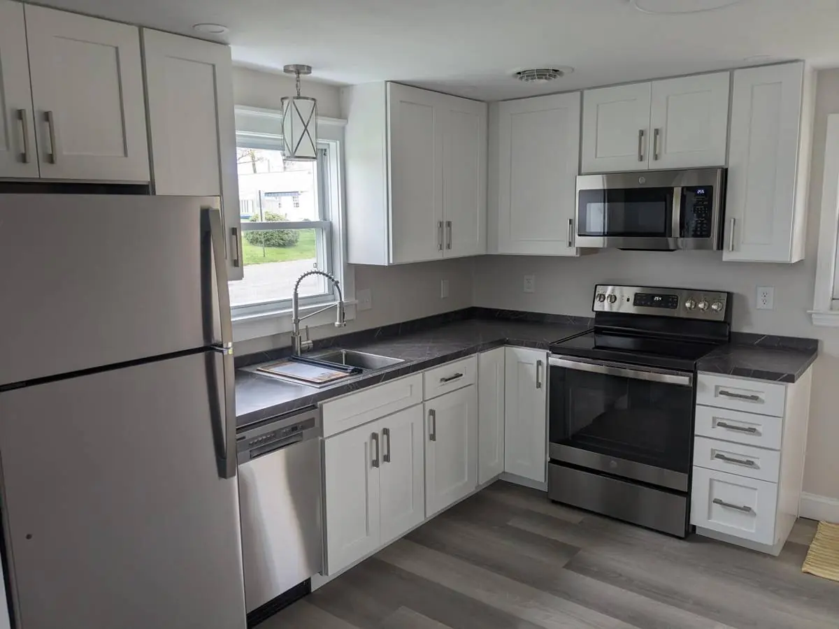 Finished L-shaped kitchen showing the range wall, microwave, dark countertops and luxury vinyl plank flooring