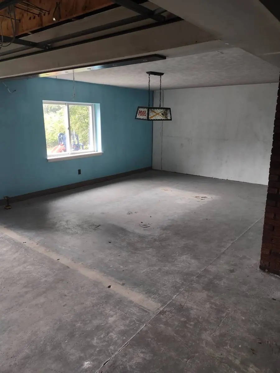 Northumberland basement before renovation, showing a bare concrete slab, painted block walls and open ceiling framing