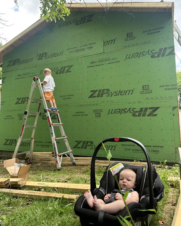 Mike Smego’s two sons on the jobsite — the older on a ladder against the new addition’s ZIP System sheathing, the baby in a car seat below