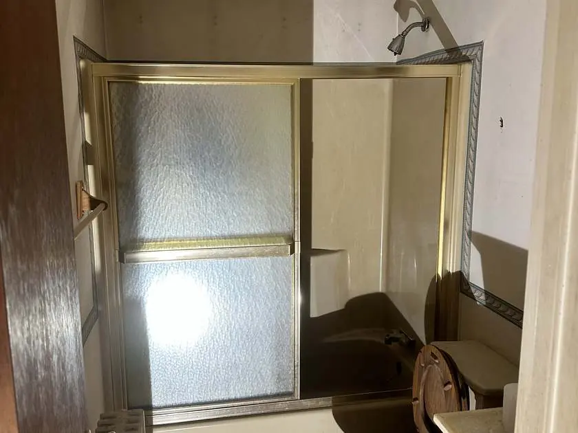 Dated bathroom with a gold-framed shower enclosure before the renovation