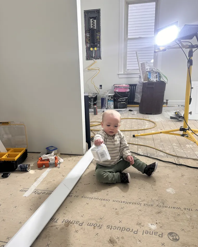 Toddler sitting on the floor underlayment beside the new electrical panel while flooring is installed
