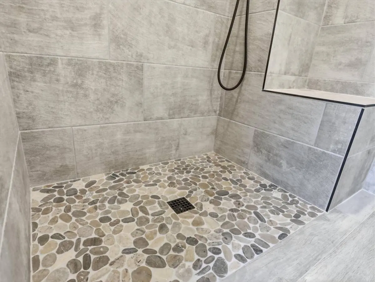 Curbless shower detail showing the pebble floor and the flush, level transition from the bathroom floor into the shower