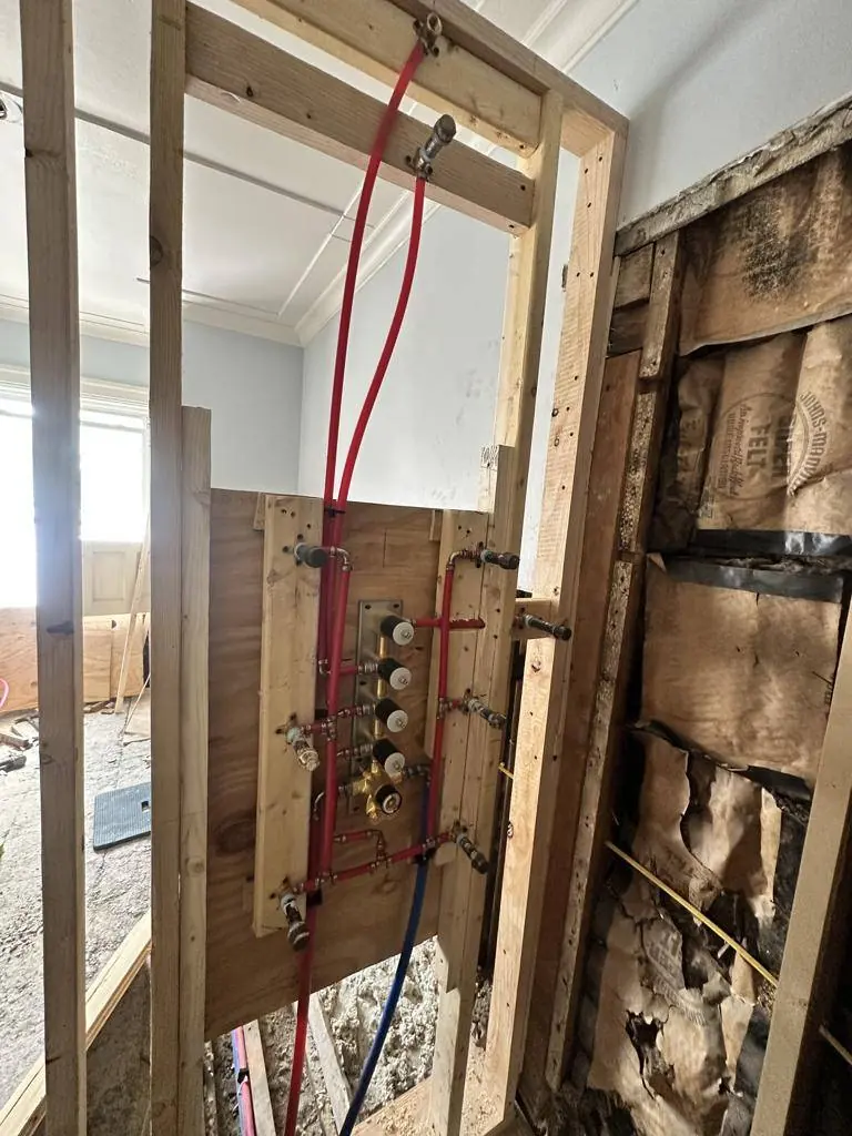 New shower valve manifold and PEX supply lines mounted on a plywood backer in the new framing