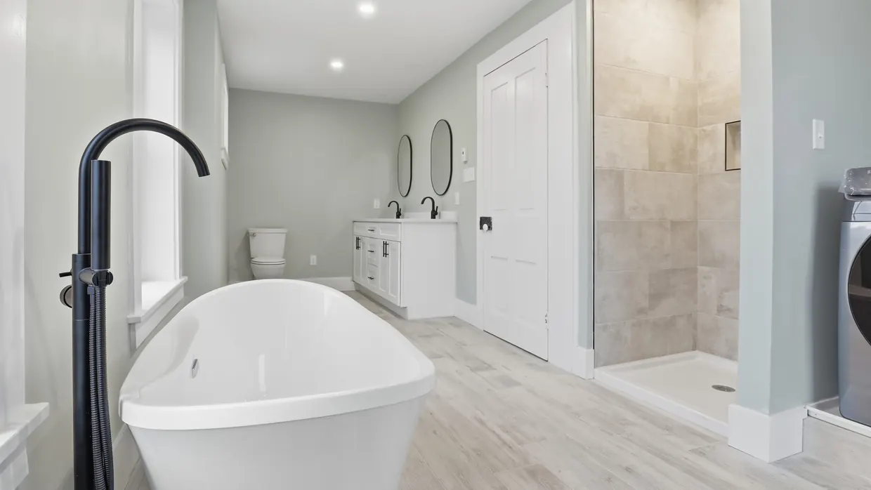 Finished primary bathroom in Central Pennsylvania with a freestanding tub, matte black floor-mounted filler, double vanity with round mirrors and a large tiled walk-in shower, by Smego Construction