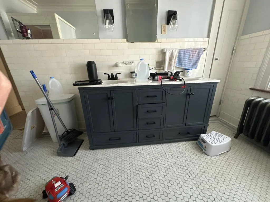 Bathroom before the remodel, with a modern vanity set against original white subway wainscot and hexagon mosaic floor