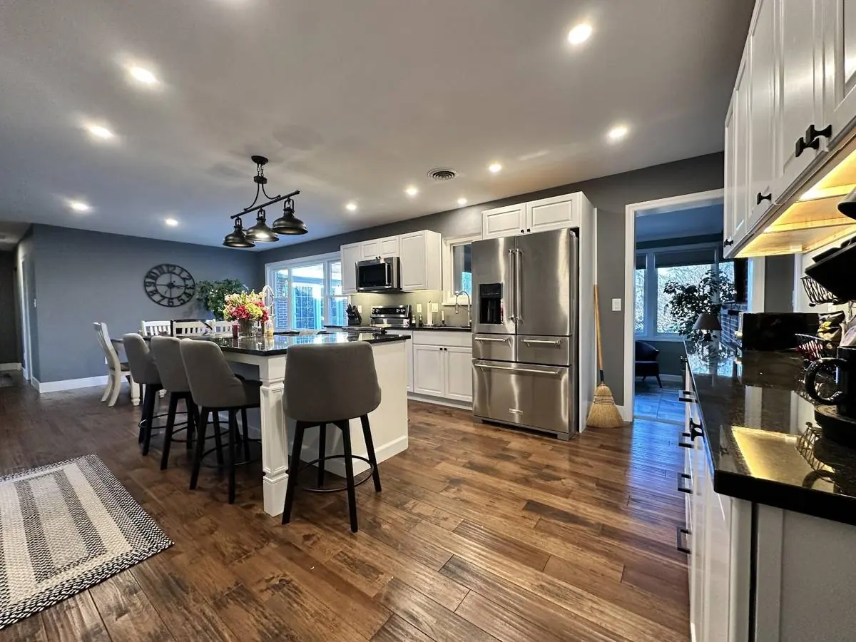 Finished open-concept kitchen remodel in Danville, Pennsylvania, with white shaker cabinets, a large island with seating, dark granite countertops and hardwood flooring running through to the dining area