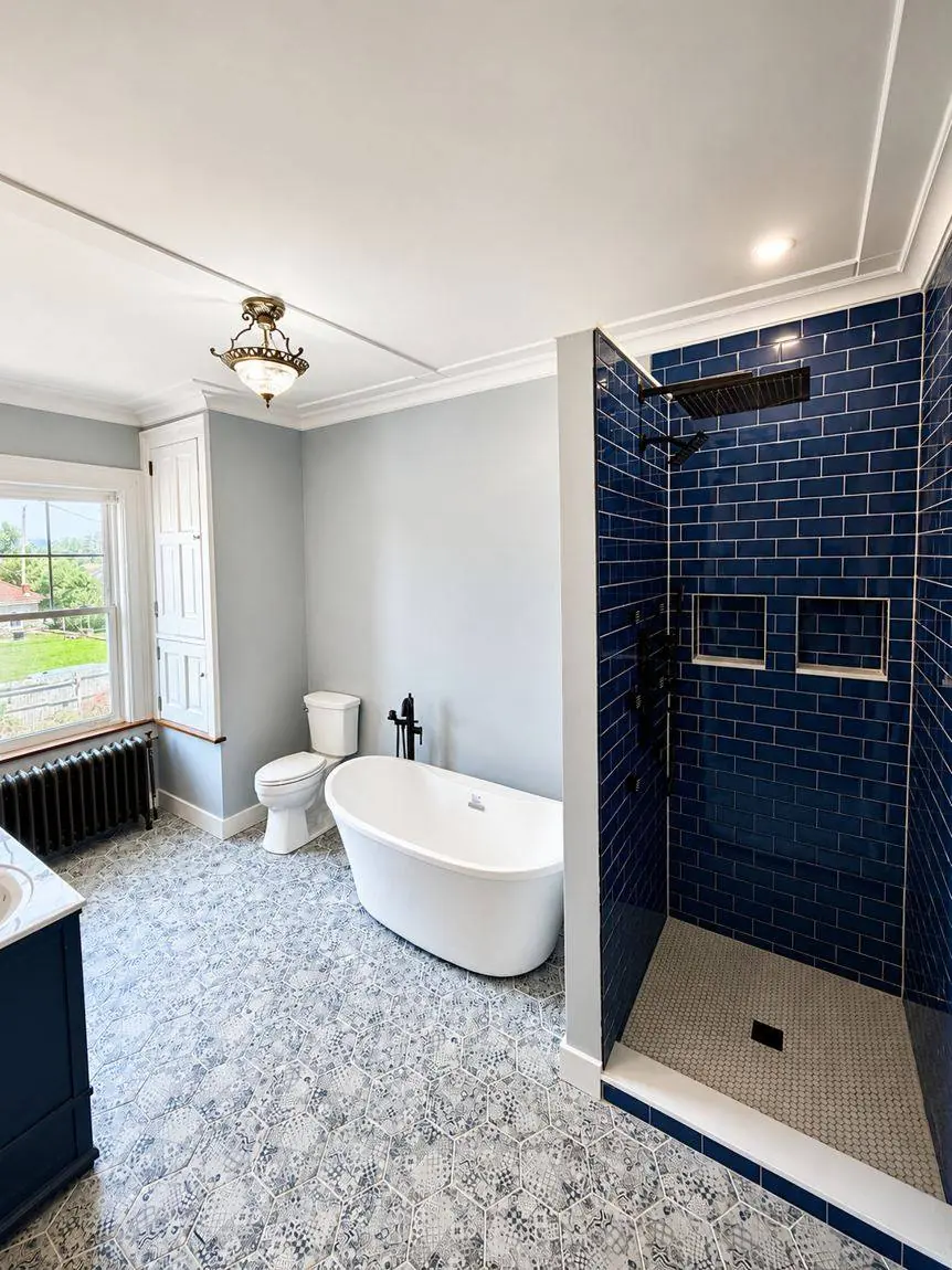 Finished bathroom showing the freestanding tub, toilet, cobalt tiled shower and the original window and radiator