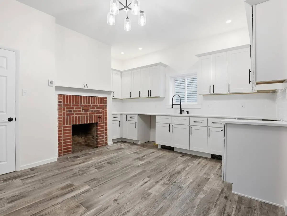Restored kitchen with quartz countertops, white cabinetry and the original brick fireplace left exposed