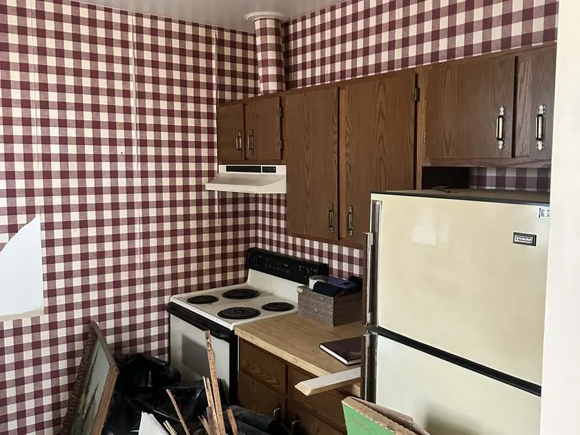 Original kitchen before renovation with red gingham wallpaper and dated brown cabinets